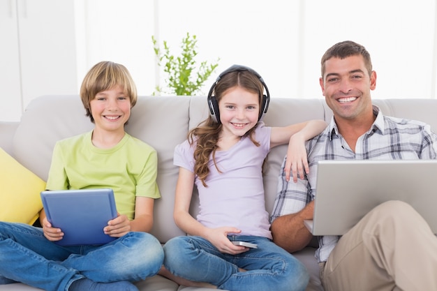 Heureux homme avec des enfants en utilisant des technologies sur le canapé
