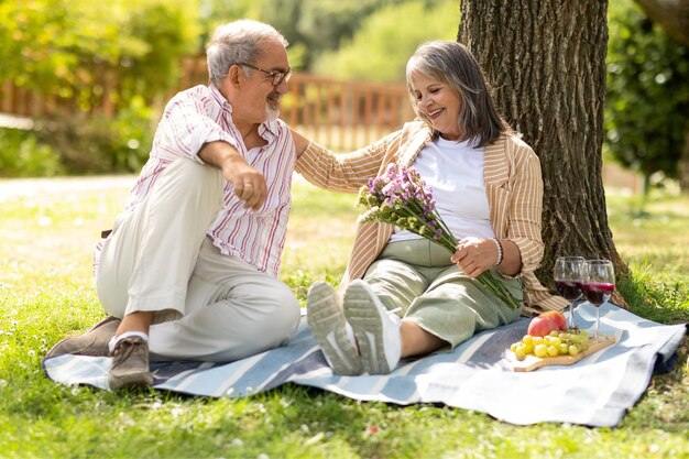 Heureux homme européen âgé donne un bouquet à une femme profitez d'un pique-nique romantique et d'un déjeuner dans le parc en plein air