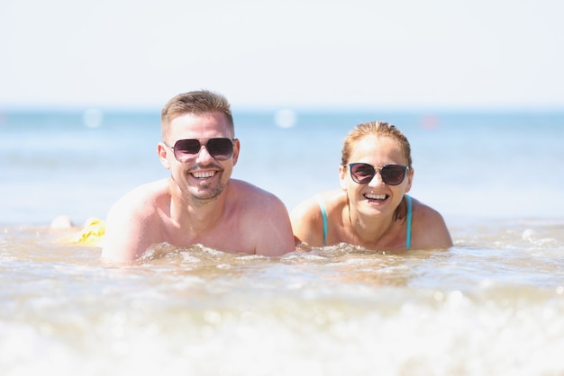 Heureux homme et femme souriants à lunettes de soleil se trouvent au bord de la mer