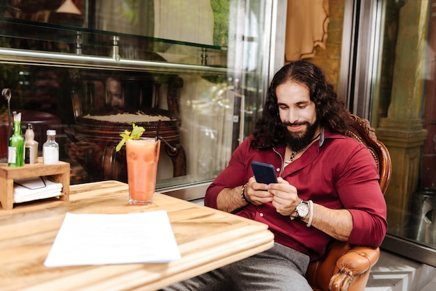 Heureux homme gentil à l'aide de son smartphone assis à la cafétéria