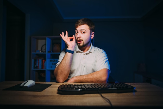 Heureux homme indépendant travaillant sur ordinateur la nuit à la maison et montrant un geste OK