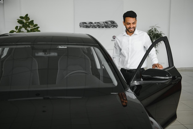 Heureux homme indien vérifiant les caractéristiques de la voiture dans la salle d'exposition