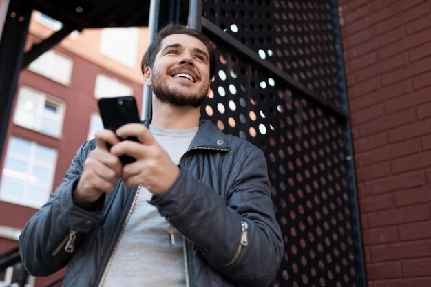 Heureux homme joyeux avec un sourire sur son visage avec un téléphone dans ses mains à l'extérieur
