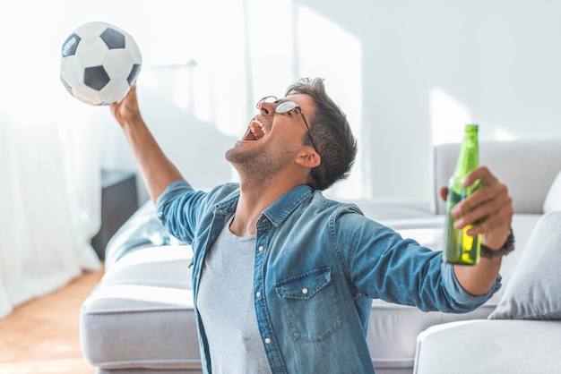 Heureux homme mûr acclamant tout en regardant un match de football sur un canapé à la maison