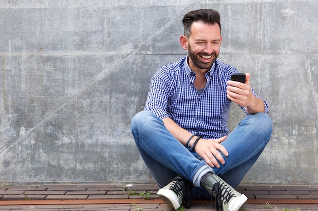 Heureux homme mûr assis à l&#39;extérieur et à l&#39;aide de téléphone portable