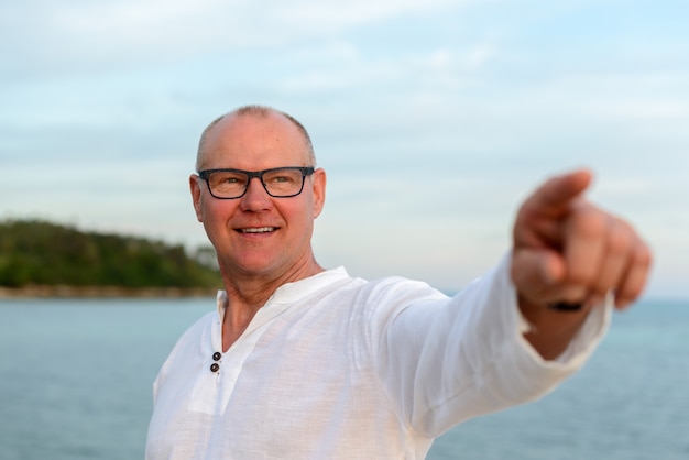 Heureux homme mûr beau touriste pointant le doigt contre vue sur la plage en plein air