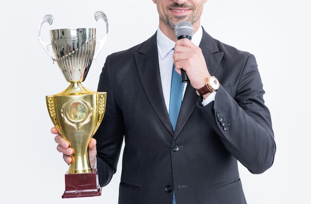 Heureux homme mûr en costume tenir la coupe du champion et microphone isolé sur fond blanc