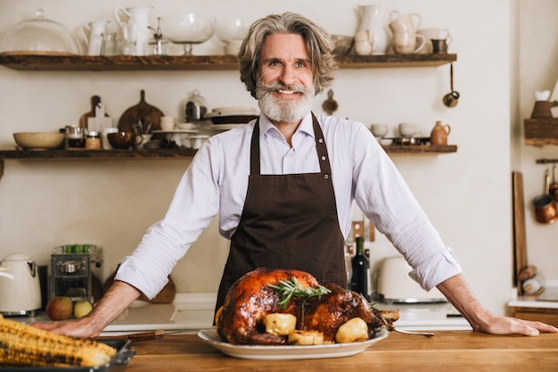 Heureux homme mûr debout à la table de Noël avec une délicieuse dinde rôtie