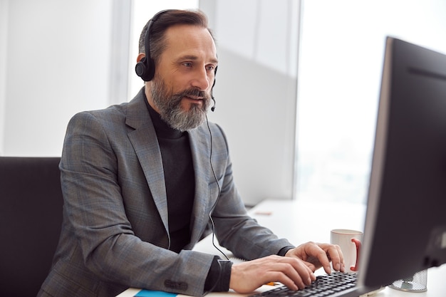 Heureux homme mûri avec un casque est assis dans un bureau blanc clair