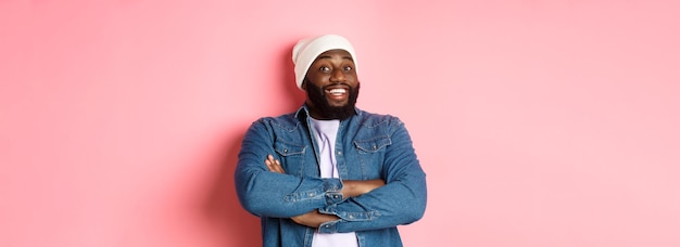 Heureux homme noir avec barbe portant bonnet et chemise en jean à la recherche intrigué et amusé de l'appareil photo smi