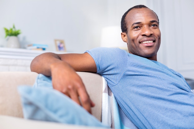 Heureux homme positif joyeux souriant et se sentant heureux tout en profitant de son temps à la maison