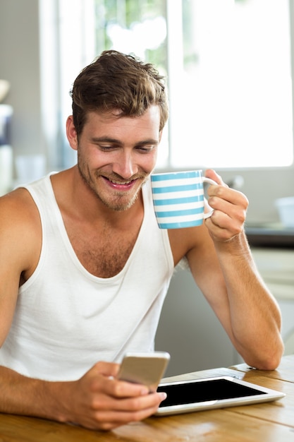 Heureux homme prenant un café tout en utilisant un téléphone portable à la maison