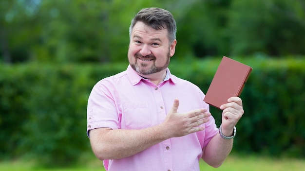 Heureux homme de race blanche intermédiaire en chemise rouge avec plaisir montre un nouveau livre