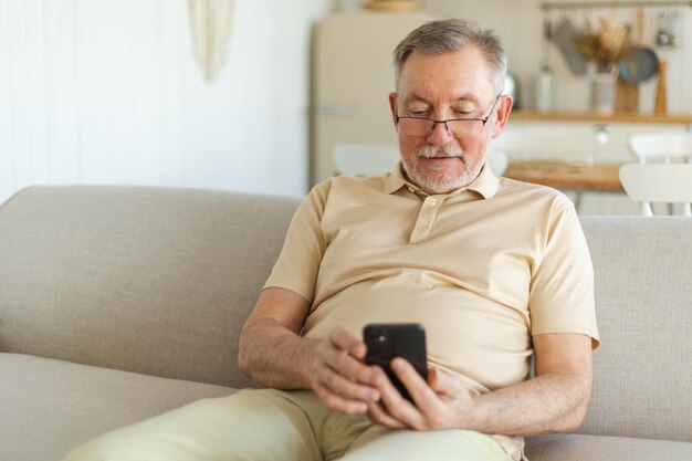 Heureux homme senior d'âge moyen tenant à l'aide d'un écran tactile de smartphone tapant la page de défilement élégant plus âgé