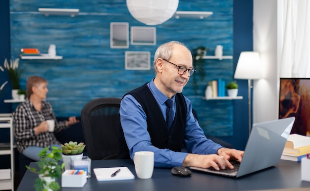 Heureux homme senior après avoir lu un e-mail avec de bonnes nouvelles assis au bureau