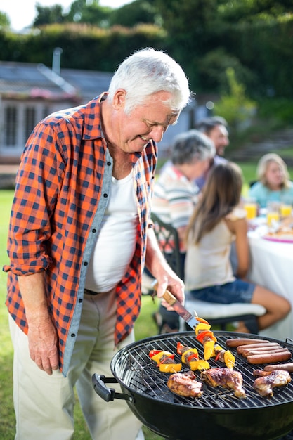 Heureux homme senior prépare des plats sur le barbecue