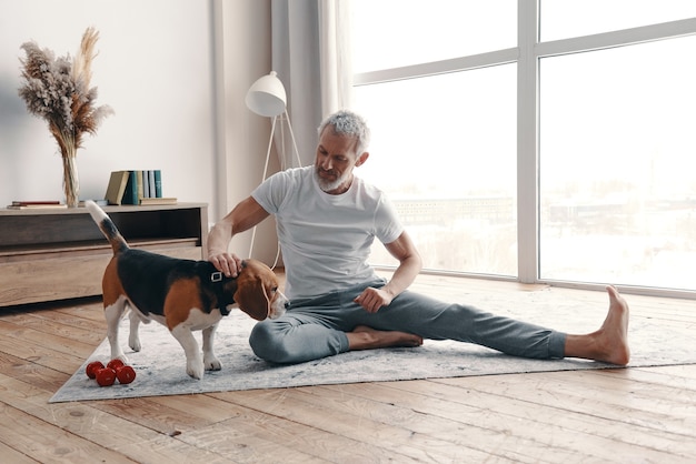 Heureux homme senior en vêtements de sport faisant de l'exercice à la maison près de son chien