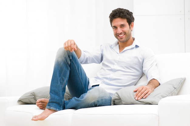 Heureux homme souriant de détente et assis sur un canapé à la maison