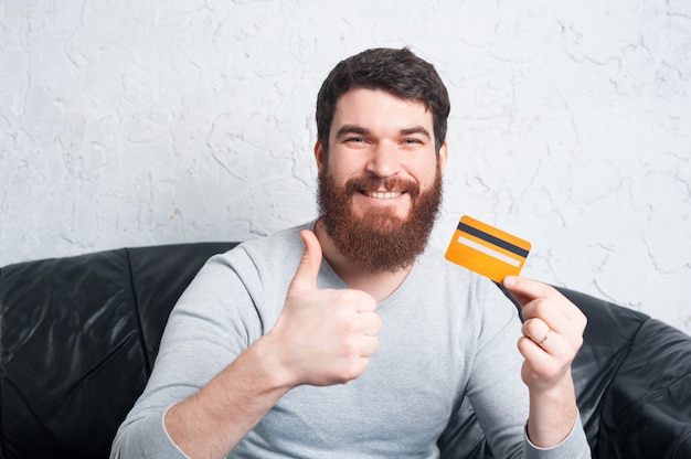 Heureux homme souriant montrant les pouces vers le haut et tenant la carte de crédit