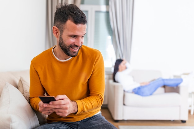 Heureux homme souriant a tourné le dos à sa femme, lisant un message sur le téléphone de son amant