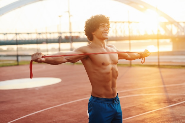 Heureux homme sportif torse nu qui s'étend de la corde tout en se tenant sur le terrain le matin