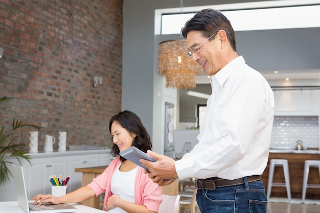 Heureux homme avec tablette à la maison pendant que sa femme enceinte travaille sur un ordinateur portable