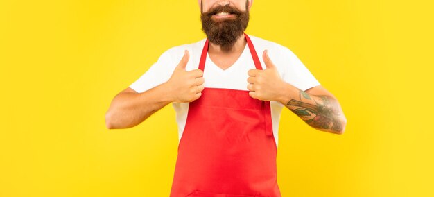 Photo heureux homme en tablier rouge donnant un service ménager à double pouce sur fond jaune