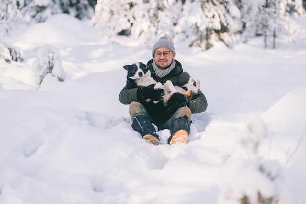 Heureux homme tenant un beau chien dans ses mains dans la forêt enneigée.