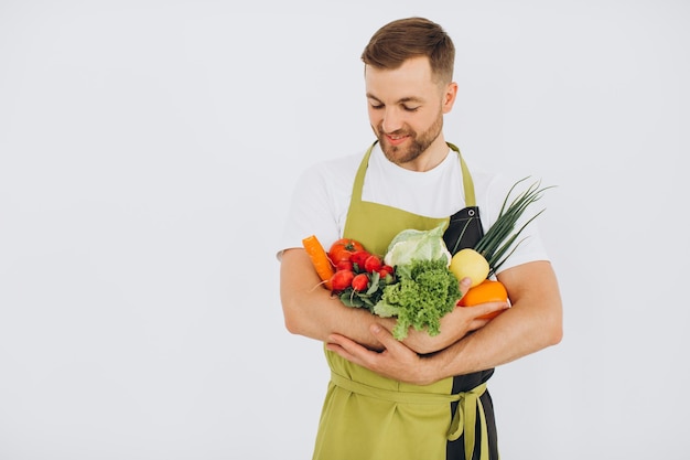 Heureux homme tenant de nombreux légumes frais différents sur fond blanc