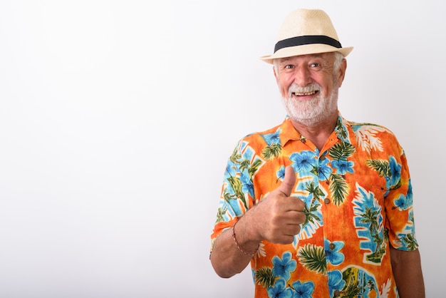 Heureux homme de touriste barbu senior souriant tout en abandonnant le pouce et portant un chapeau sur blanc