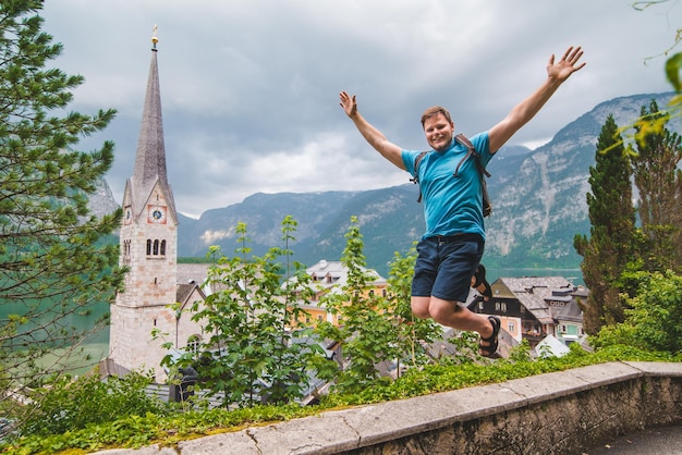 Heureux homme touriste debout avec les mains levées regardant la ville de hallstatt d'en haut