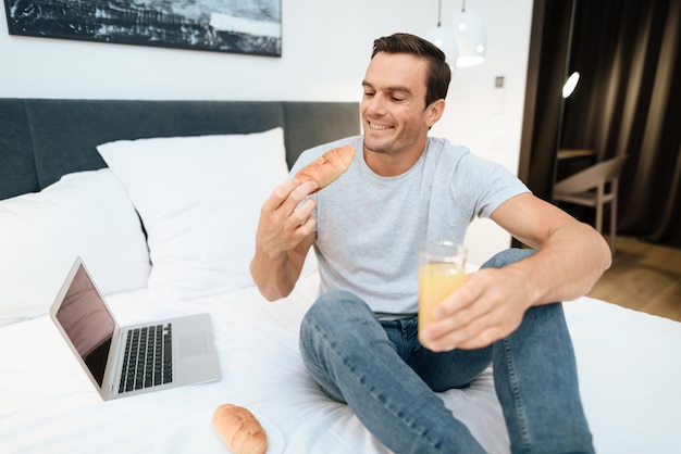 Heureux homme travaillant et prenant son petit déjeuner au lit