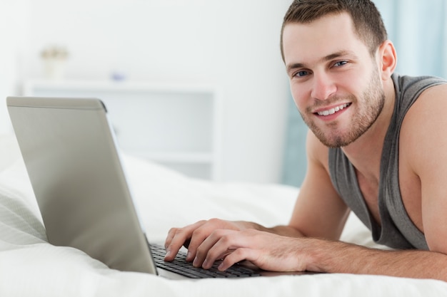 Heureux homme utilisant un ordinateur portable en position couchée sur le ventre