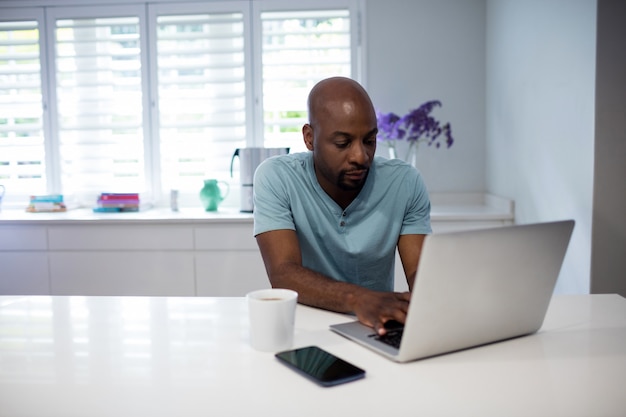 Heureux homme utilisant un ordinateur portable avec un téléphone mobile et une tasse de café sur la table