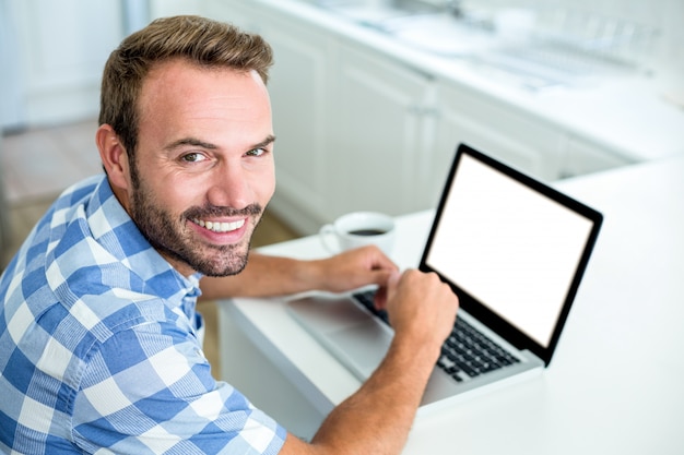 Heureux homme utilisant un ordinateur portable tout en étant assis à table dans la cuisine