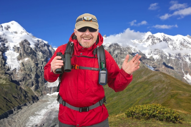 Heureux homme voyageur avec des jumelles à la main sur les montagnes enneigées