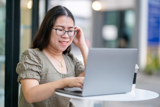 Heureux des indépendants asiatiques d'affaires féminins occasionnels travaillant avec un ordinateur portable avec une tasse de café et un smartphone dans un café comme le concept de communication d'arrière-plan