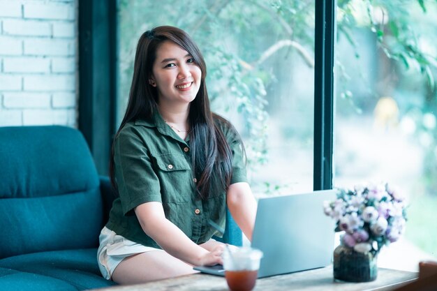 Heureux des indépendants asiatiques d'affaires féminins occasionnels travaillant avec un ordinateur portable avec une tasse de café et un smartphone dans un café comme le concept de communication d'arrière-plan