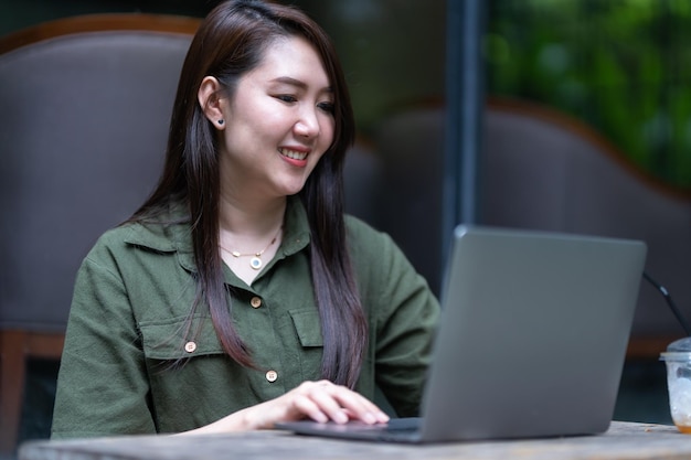 Heureux des indépendants asiatiques d'affaires féminins occasionnels travaillant avec un ordinateur portable avec une tasse de café et un smartphone dans un café comme le concept de communication d'arrière-plan