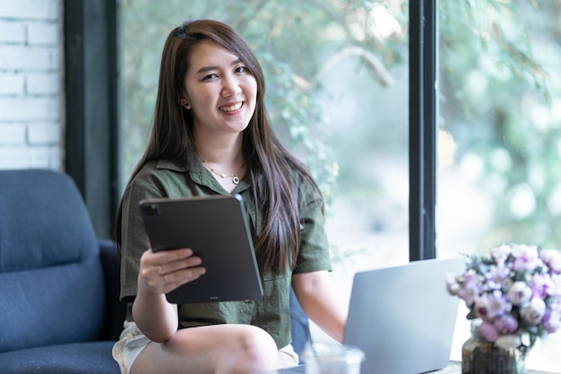 Heureux des indépendants asiatiques d'affaires féminins occasionnels travaillant avec un ordinateur portable et utilisant une tablette avec une tasse de café et un smartphone dans un café comme le concept de communication d'arrière-plan