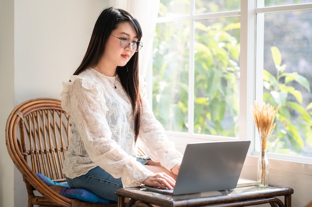 Heureux des indépendants asiatiques d'affaires femme décontractée travaillant avec un ordinateur portable avec une tasse à café et un smartphone dans un café comme l'arrière-plan, concept de communication