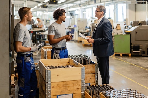 Heureux inspecteur de contrôle de la qualité communiquant avec de jeunes travailleurs manuels dans une usine sidérurgique