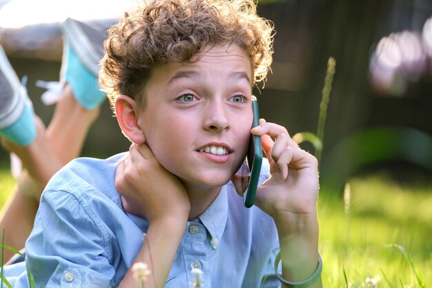 Heureux jeune adolescent parlant sur téléphone portable à l'extérieur dans le parc d'été. Concept d'amitié en ligne.