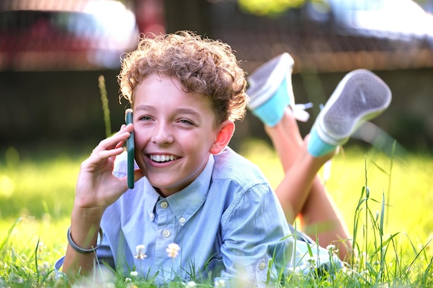 Heureux jeune adolescent parlant sur téléphone portable à l'extérieur dans le parc d'été Concept d'amitié en ligne