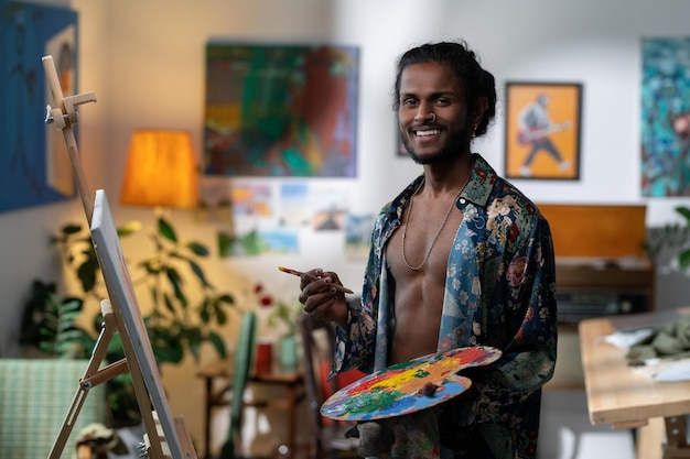 Heureux jeune artiste masculin avec pinceau et palette de couleurs regardant la caméra