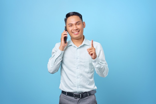 Heureux jeune bel homme d'affaires parlant au téléphone portable et pointant le doigt vers le haut avec une idée