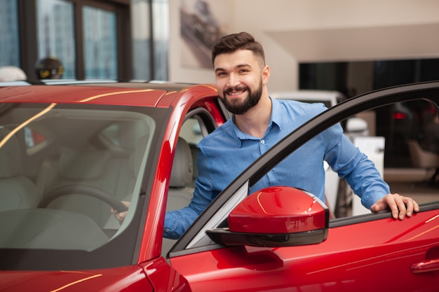 Heureux jeune bel homme entrer dans la voiture au salon de la concession.