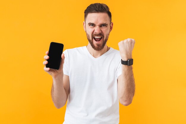 un heureux jeune bel homme posant isolé sur un mur jaune montrant l'affichage du téléphone portable