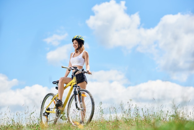 Heureux jeune cavalière à vélo à vélo jaune sur l'herbe