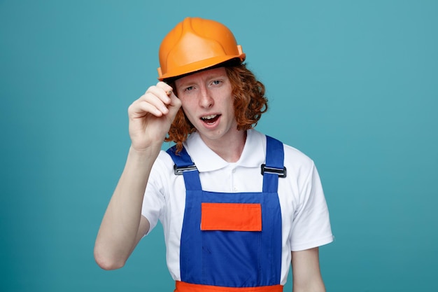 Heureux jeune constructeur homme en uniforme tenant un stylo marqueur à la caméra isolé sur fond bleu